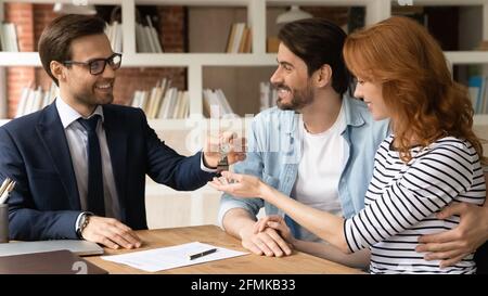 Felice coppia millennial ricevere le chiavi da realtor, l'acquisto di beni immobili Foto Stock