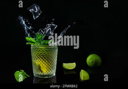 Rinfrescante cocktail mojito con cubetti di ghiaccio e spruzzi su sfondo scuro. Bevanda estiva con lime fresche e menta con spazio copia. Foto Stock