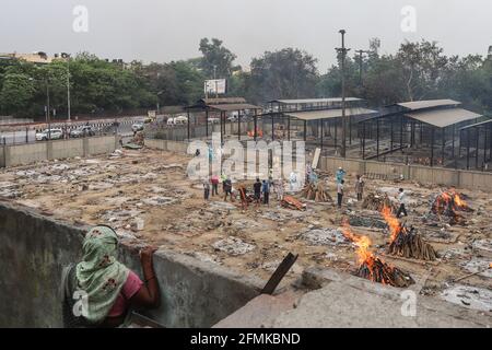 Delhi, India. 09 maggio 2021. Una donna guarda i parenti delle vittime del coronavirus (Covid-19) che eseguono gli ultimi riti durante una cremazione ad un crematorio a Nuova Delhi. L'India riporta 3, 66,161 nuovi casi, 3,754 decessi nelle ultime 24 ore. Credit: SOPA Images Limited/Alamy Live News Foto Stock