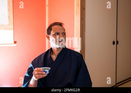 Tradizionale giapponese machiya casa ryokan con l'uomo in kimono da alcova e carta appesa scroll bere tè verde Foto Stock