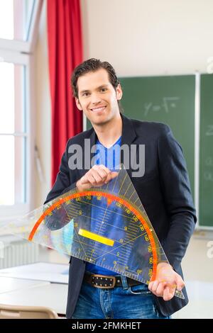 Insegnante o docente nella scuola in possesso di un triangolo geometria di fronte a una lavagna nella classe della scuola Foto Stock