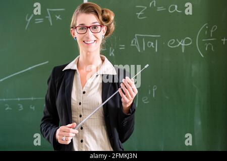 Insegnante o docente a scuola che tiene un puntatore davanti di una lavagna in classe scolastica Foto Stock