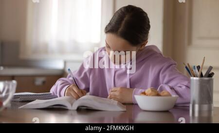 Giovane ragazza concentrata che studia da sola in cucina moderna. Foto Stock