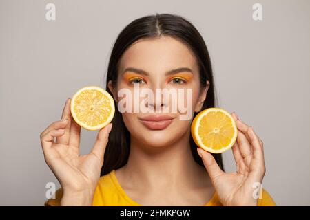 Giovane bel modello sano con pelle chiara e capelli lisci che tengono frutta di limone su sfondo bianco ritratto. Dieta, cura della pelle e trattamento del viso Foto Stock