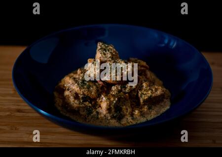 Pollo burro masala curry in una ciotola blu guarnito con foglie tritate verdi con sfondo di legno Foto Stock
