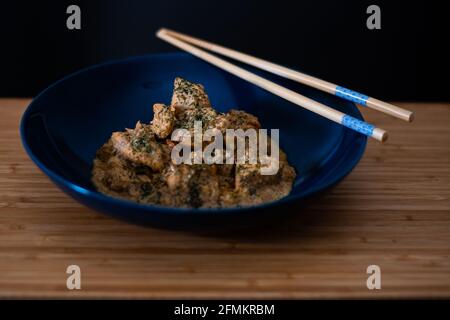 Succulento delizioso pollo burro masala curry in un blu ciotola guarnita con foglie verdi tritate con fondo di legno e bastone Foto Stock