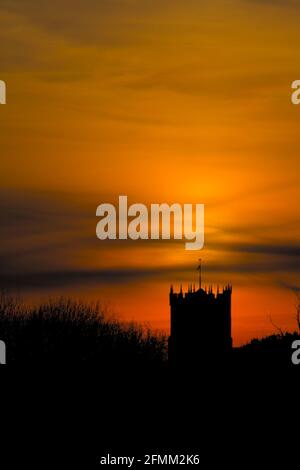 Silhouette del 15 ° secolo Torre di Christchurch Priory, Regno Unito, contro il cielo rosso arancione di UN tramonto Regno Unito Foto Stock