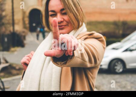 Donna sorridente felice. Una sola donna che flirta e si inarchia un occhio, puntando il dito verso l'alto, fuoco selettivo sul dito, fotografia sfocata, rumore della pellicola Foto Stock