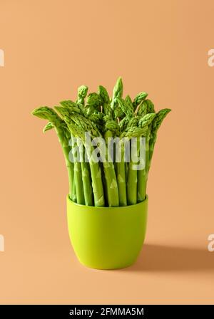 Mazzo di asparagi crudi in una pentola verde di ceramica su fondo beige. Asparagi verdi freschi su sfondo colorato. Foto Stock