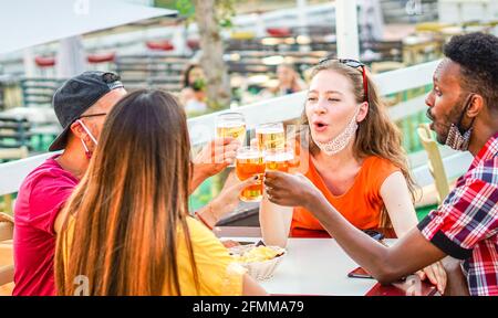 Amici multirazziali che si acclamano con la birra e sorridono ridendo con ciascuno Altro concetto di maschera facciale di Coronavirus Foto Stock