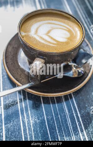 Tazza di caffè fresco con disegno floreale in schiuma. Tavolo di legno scuro come sfondo Foto Stock