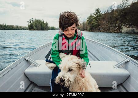 Ragazzo e cane seduto in una barca di metallo che viaggia su un lago. Foto Stock