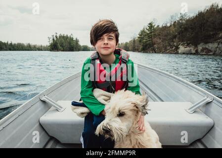 Ragazzo e cane seduto in una barca di metallo che viaggia su un lago. Foto Stock