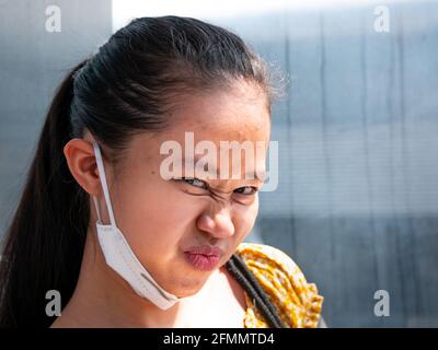 Medellin, Antioquia, Colombia - Marzo 27 2021: Giovane donna asiatica con una maschera facciale sotto la bocca sorride e guarda la fotocamera Foto Stock