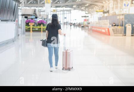 Donna asiatica che trasporta valigia e indossa una maschera chirurgica, prepara il check-in per ottenere la carta d'imbarco all'aeroporto. Durante il Covid- Foto Stock