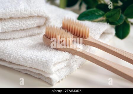 Spazzolini da denti in bambù, asciugamani e foglie di piante verdi in bagno Foto Stock