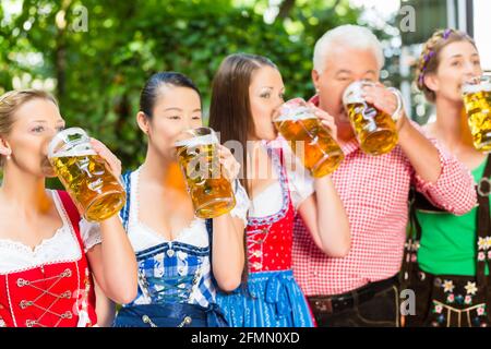 Nel giardino della birra - amici, l uomo e la donna in Tracht, Dirndl e lederhosen bere una birra fresca in Baviera, Germania Foto Stock