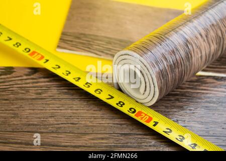 Metro a nastro in linoleum e coltello su fondo isolato. Un pezzo di linoleum. Misurazione e taglio del linoleum. Linoleum per pavimenti in PVC. Galleggiamento domestico Foto Stock