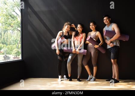 Felice uomo sorridente e donne che si divertono a parlare in palestra. Gruppo di giovani che si rilassano in palestra dopo l'allenamento con fondo nero - Full Length Body Foto Stock