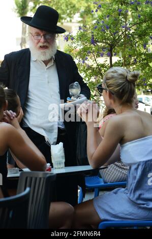 Un ebreo ortodosso israeliano si avvicina alle donne laiche israeliane in un caffè all'aperto a Tel-Aviv, Israele. Foto Stock