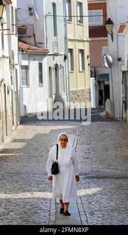 Una suora cattolica che cammina tra i vecchi edifici di Cascais, Portogallo. Foto Stock