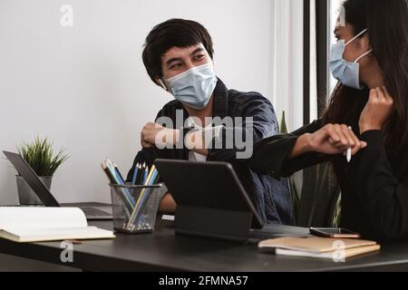 Due giovani colleghi di affari diversi che indossano maschere di protezione del viso che urtano i gomiti, salutarsi mentre lavorano durante la quarantena covid 19. Foto Stock