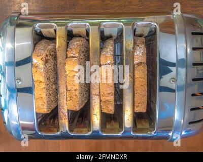 Primo piano POV di quattro fette di pane marrone fresco nelle quattro fessure di un tostapane in acciaio retrò, pronto per la tostatura. Foto Stock