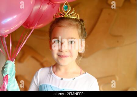 carino piccolo caucasico sette anni bambina a casa in un costume elsa congelato con una corona d'oro e. palloncini rosa festeggia allegramente la sua b Foto Stock