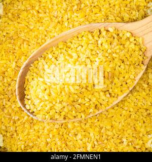 vista dall'alto del bulgur crudo (frumento parboiled cracked) goods in cucchiaio di legno closeup Foto Stock