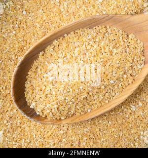 vista dall'alto delle semole di grano grezzo (grani di grano lucidati frantumati) in un cucchiaio di legno closeup Foto Stock