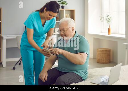 Operatore sanitario che insegna al paziente anziano di utilizzare l'app per la salute sul suo telefono cellulare Foto Stock