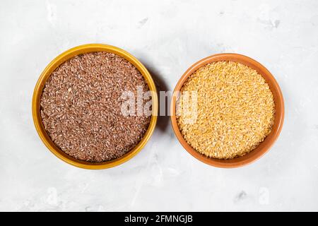 vista dall'alto dei semi di lino marroni e dorati, rotondi ciotole in ceramica su tavola in cemento grigio Foto Stock