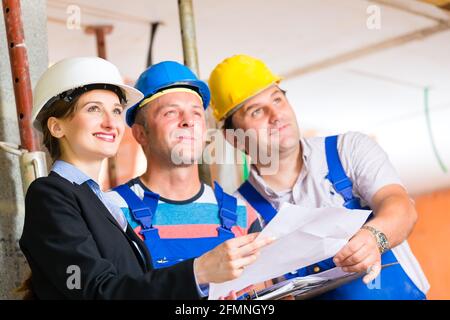 Sito in costruzione di un team o di un architetto e costruttore o lavoratore con i caschi di controllo o di discussione del piano o Cianografia Foto Stock