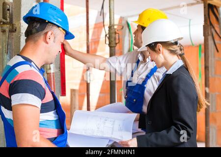 Sito in costruzione di un team o di un architetto e costruttore o lavoratore con i caschi di controllo o di discussione del piano o Cianografia Foto Stock