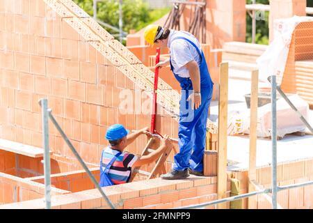 Due builder o lavoratore con caschi controllare pareti in impalcatura con una livella a bolla sulla costruzione e sul sito in costruzione Foto Stock