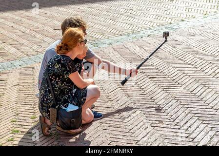 SIENA, ITALIA - 27 agosto 2020: Una famiglia con gentile piegarsi e scattare una foto di se stessi in vacanza con l'aiuto di un bastone selfie su un p pari Foto Stock