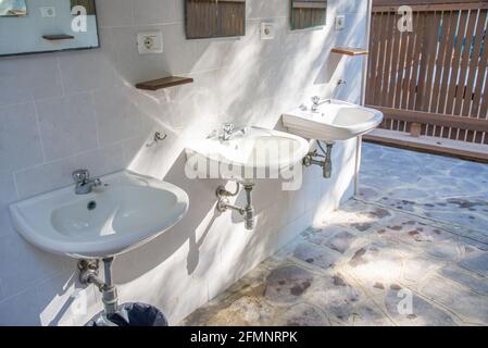 PISA, ITALY - 22 ago 2020: Pisa, Toscana/Italy - 22.08.2020: Tre lavandini in ceramica con rubinetti per acqua fredda, specchio, prese e ripiani in un ro piastrellato Foto Stock