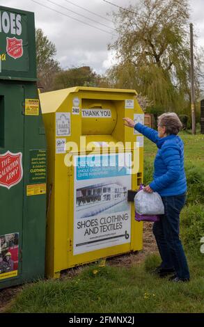 Hampshire, Inghilterra, Regno Unito. 2021. Donna che dona vestiti per beneficenza usando un contenitore di raccolta della comunità per beneficenza in un villaggio dell'Hampshire. Foto Stock