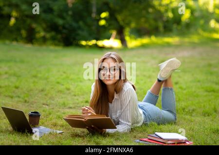 Concetto di apprendimento. Smiling Student Girl in Eyeglasses leggere Libro mentre studia all'aperto Foto Stock