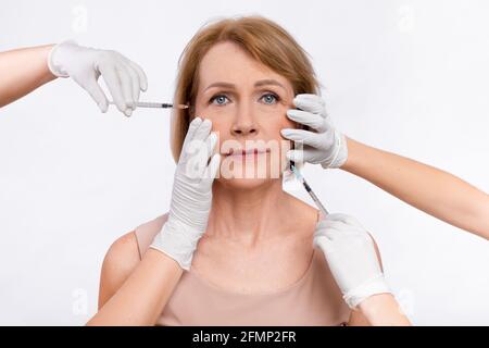 Ringiovanimento della pelle maturo. Donna anziana che riceve un trattamento cosmetico con iniezioni di bellezza sullo sfondo di studio luminoso Foto Stock