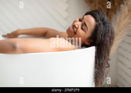 Donna nera che prende il bagno distendendosi nella vasca da bagno in bagno Foto Stock