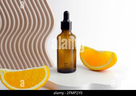 Siero in flacone di vetro con pipetta. Olio naturale essenziale su un podio bianco. Imballaggio per un prodotto cosmetico. Oli con estratto di arancia Foto Stock