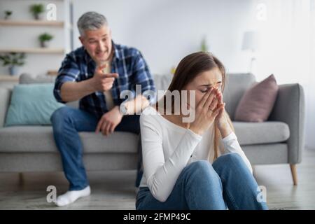 Donna matura seduta sul pavimento e piangendo, suo marito accusandola o accusandola a casa Foto Stock
