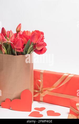 Bellissimi tulipani rossi in una borsa regalo e confezioni regalo. Verticale congratulatorio foto buon compleanno, giorno di San Valentino, Festa della mamma. Foto Stock
