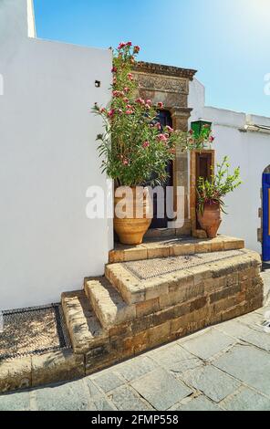 Strette strade ripide con case bianche pareti e cespugli fioriti E vecchie scale nella storica città greca Lindos sotto il blu cielo Foto Stock