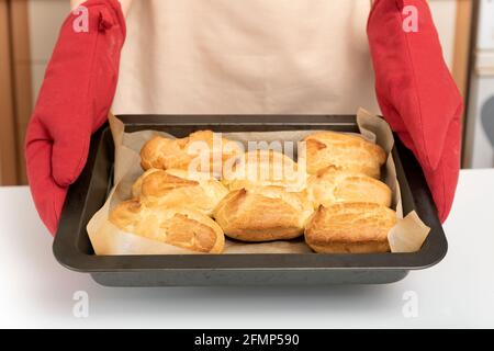 Cuocete in forno il mitt tiene la lastra di cottura delle focaccine. Profiteroles, puffs, popover, eclair Foto Stock