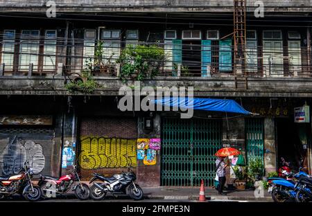 Un uomo con un ombrello rosso cammina davanti a un vecchio edificio rivestito di graffiti nella zona di Chinatown a Bangkok, Thailandia Foto Stock