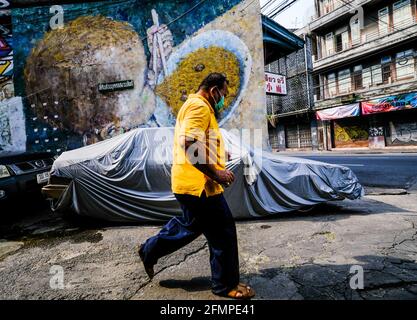 Un uomo che indossa una maschera e una polo gialla cammina davanti a un gigantesco murale nella zona di Chinatown a Bangkok, Thailandia Foto Stock