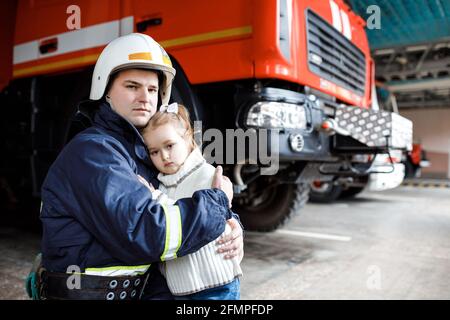 Bravissimo pompiere in uniforme che tiene in piedi una bambina salvata sfondo nero Foto Stock
