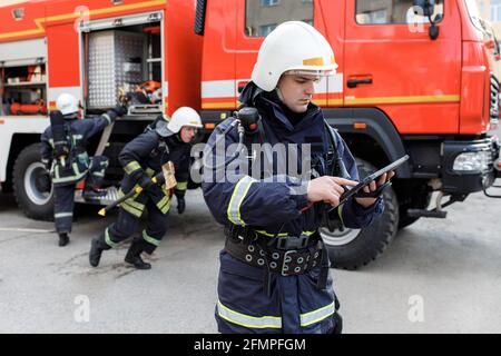 Ritratto di pompieri in attività di lotta antincendio, vigili del fuoco in indumenti protettivi e casco utilizzando tablet computer in azione combattimenti Foto Stock